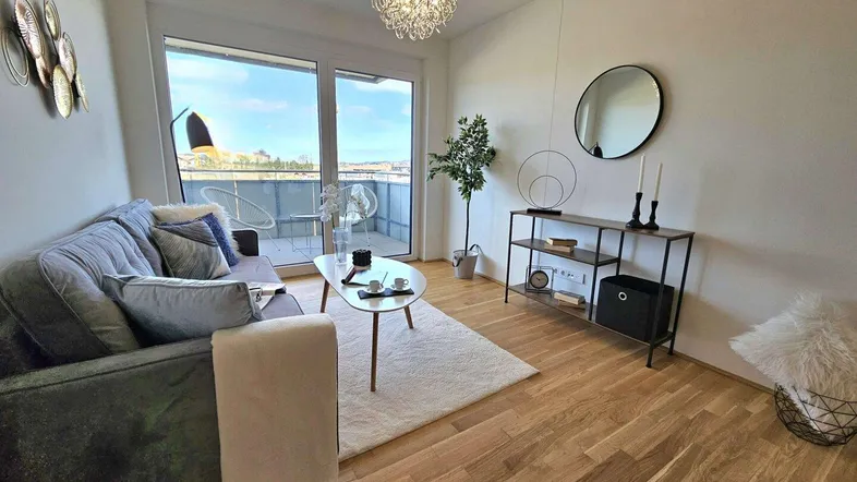 Helles Wohnzimmer mit Holzboden, modernem Sofa und Zugang zum Balkon, ideal für Entspannung.