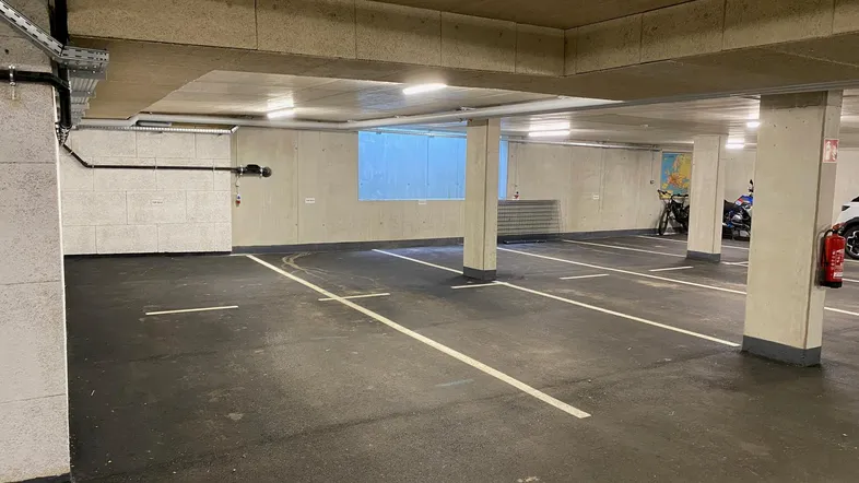 Geräumige Tiefgarage mit markierten Parkplätzen, Betonwänden und Fahrradabstellbereich.