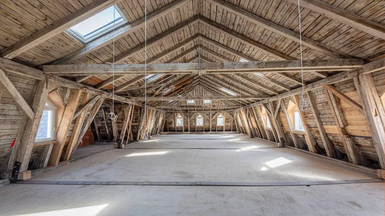 Großer, unfertiger Dachboden mit sichtbaren Holzbalken und Dachfenstern, bereit für den Ausbau.