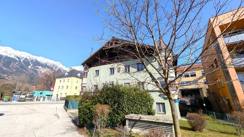 Gebäudeansicht mit grüner Fassade und schneebedeckten Bergen im Hintergrund unter blauem Himmel.