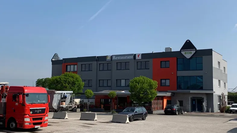 Modernes Gewerbegebäude mit Restaurant, Parkplätzen und einer auffälligen Fassadengestaltung unter blauem Himmel.