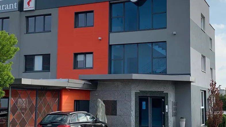 Modernes Gewerbegebäude mit markanter orangefarbener Fassadenakzentuierung und Parkplatz für Kunden.