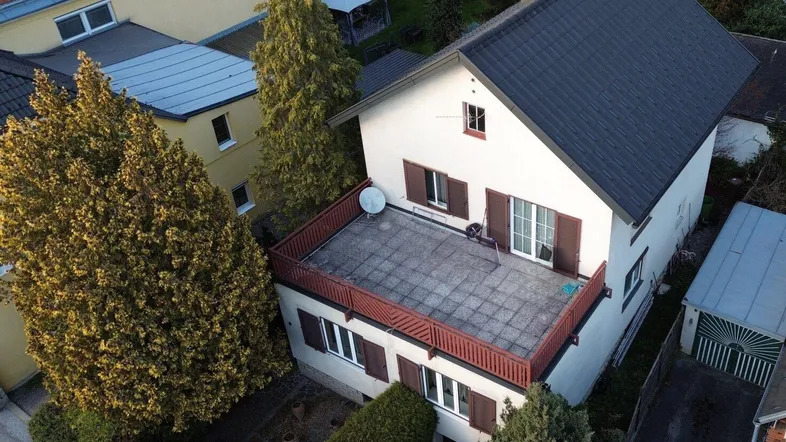 Luftaufnahme eines Hauses mit großer Dachterrasse und umliegenden Gebäuden.
