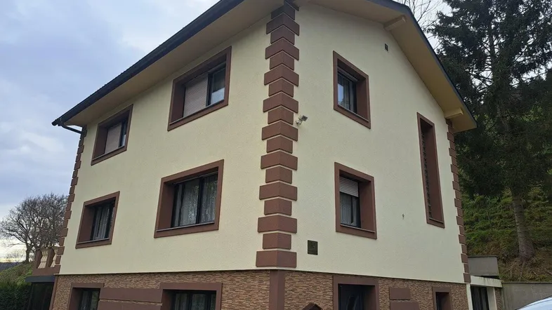 Traditionelles Einfamilienhaus mit beiger Fassade, braunen Akzenten und Satteldach in ländlicher Umgebung.
