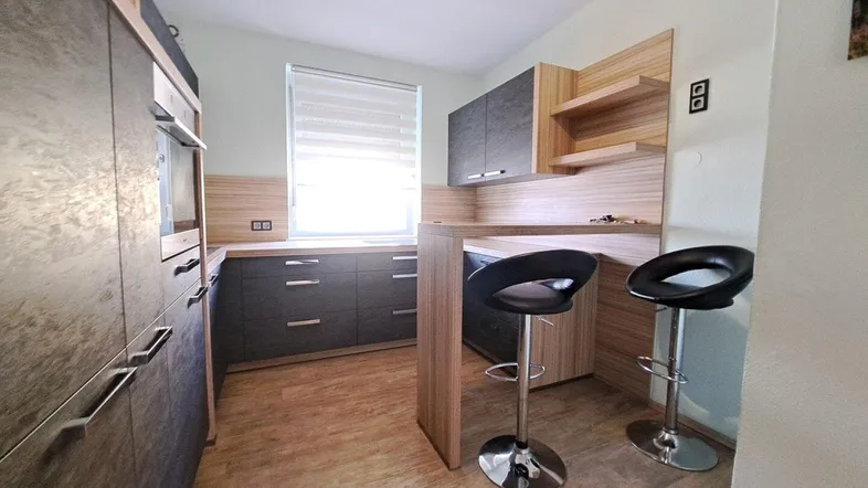 Moderne Küche mit dunklen Schränken, Holzdetails, integriertem Backofen und einer Frühstücksbar mit Hockern.