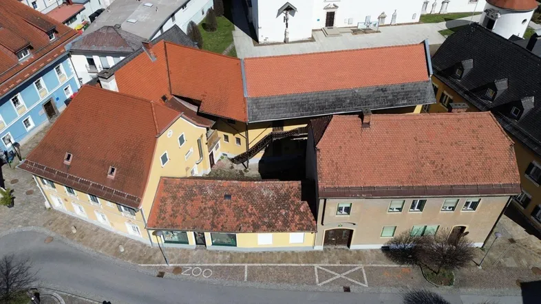 Luftaufnahme eines historischen Gebäudekomplexes mit mehreren Dächern in einer städtischen Umgebung.