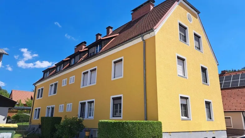 Gelbes Mehrfamilienhaus mit Satteldach und vielen Fenstern unter blauem Himmel.