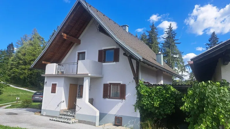 Haus mit Giebeldach und kleinem Balkon in ländlicher Umgebung unter blauem Himmel.