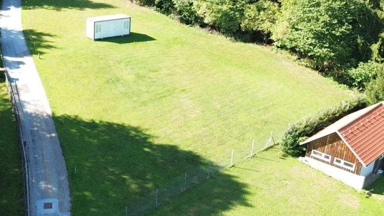 Luftaufnahme eines weitläufigen grünen Grundstücks mit einem kleinen Gebäude und angrenzendem Wald.