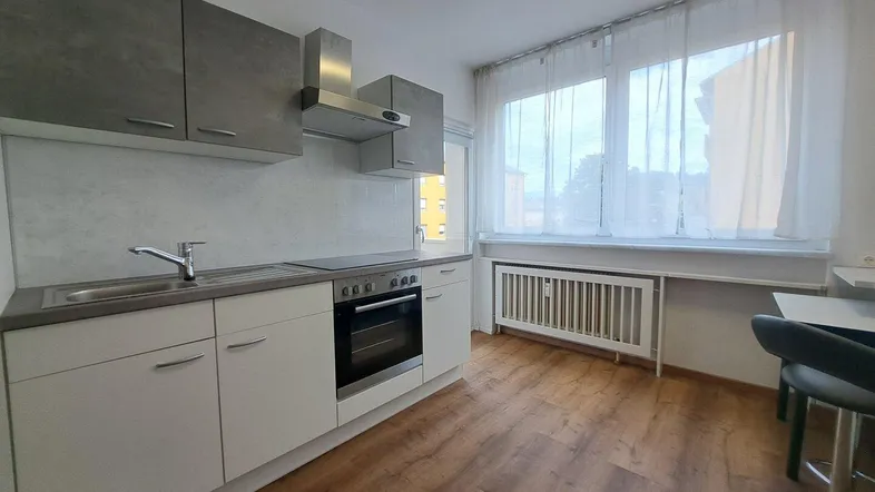 Moderne Küche mit hellen Schränken, integriertem Backofen und großem Fenster für viel Tageslicht.