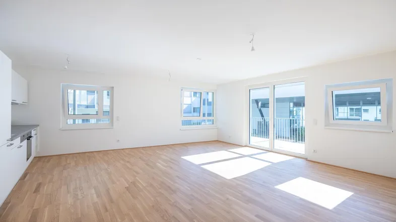 Heller, offener Wohn- und Essbereich mit Parkettboden und Zugang zum Balkon, bereit zur Einrichtung.