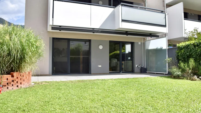 Gepflegter Gartenbereich mit Rasenfläche und Terrasse im Erdgeschoss eines modernen Gebäudes.