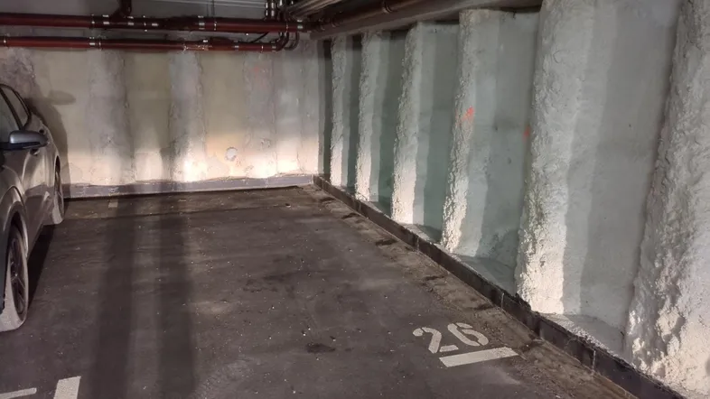 Tiefgaragenstellplatz mit Betonwänden und sichtbaren Leitungen an der Decke.