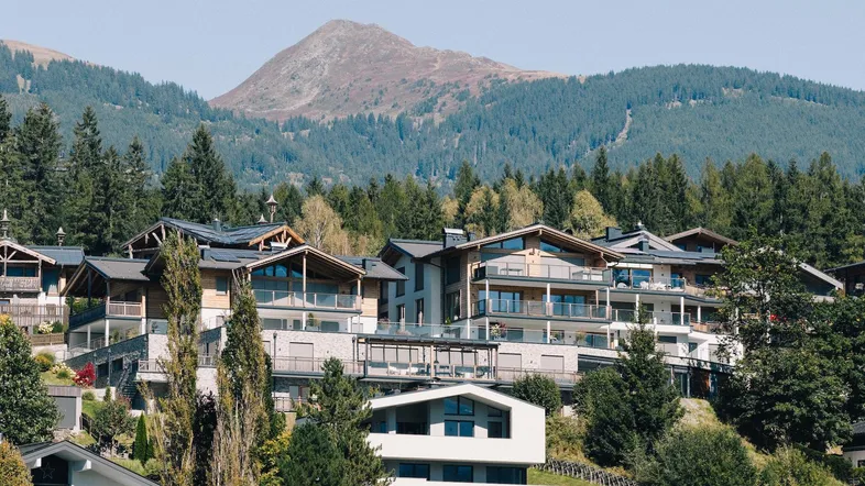 Moderne Gebäude in einer malerischen Berglandschaft mit üppigem Grün und klarem Himmel.