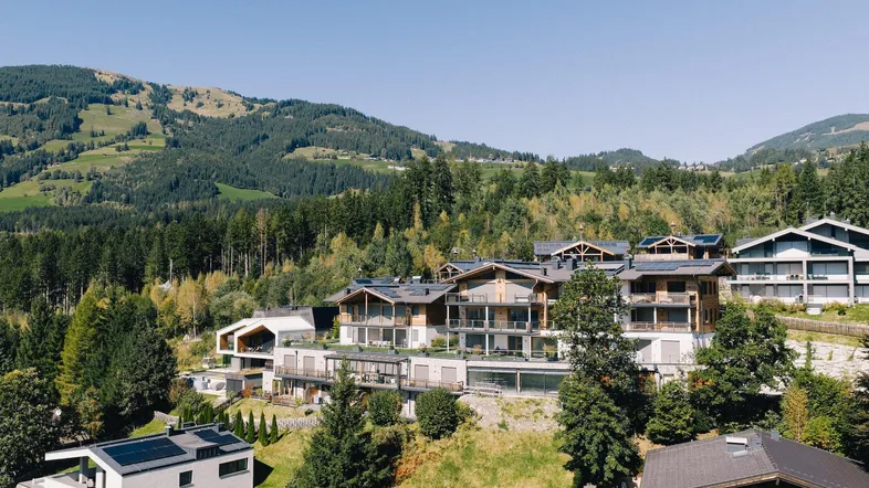Panoramablick auf eine moderne Wohnanlage in den Bergen mit viel Grün und Wald.