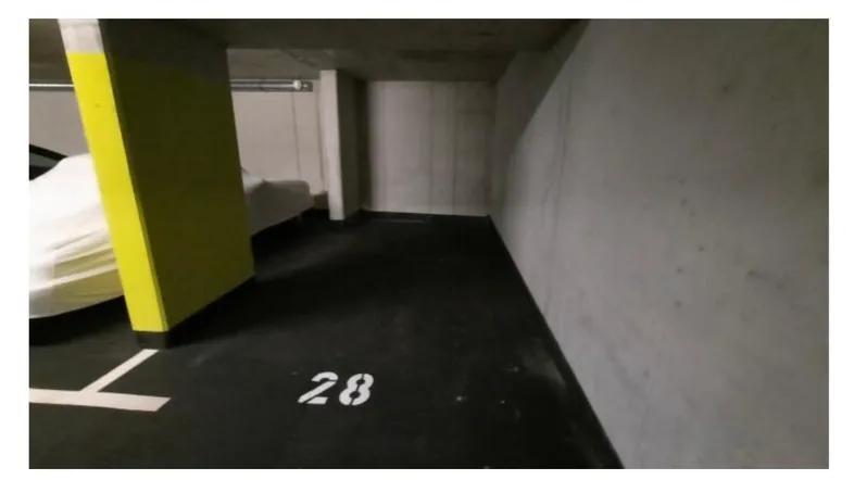 Einzelner Tiefgaragenstellplatz Nummer 28 mit Betonwänden und gelbem Pfeiler.