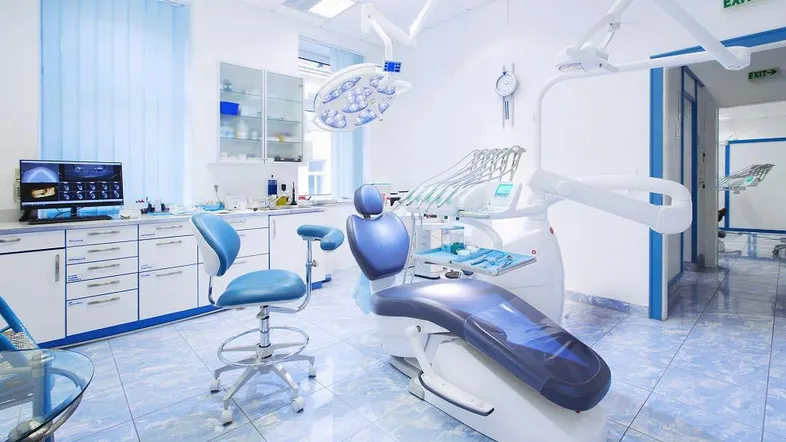 Moderner zahnmedizinischer Behandlungsraum mit blauen Akzenten, Fliesenboden und professioneller Ausstattung.