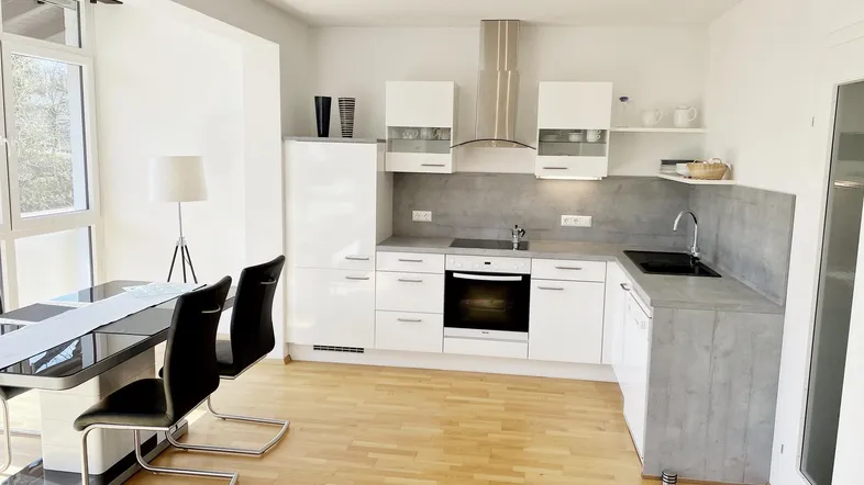 Moderne offene Küche mit weißen Hochglanzfronten, grauer Arbeitsplatte und hellem Holzboden, kombiniert mit einem Essbereich.