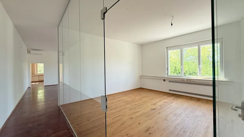 Helles Büro mit Glaswänden und Holzboden, bietet viel natürliches Licht und eine moderne Arbeitsumgebung.