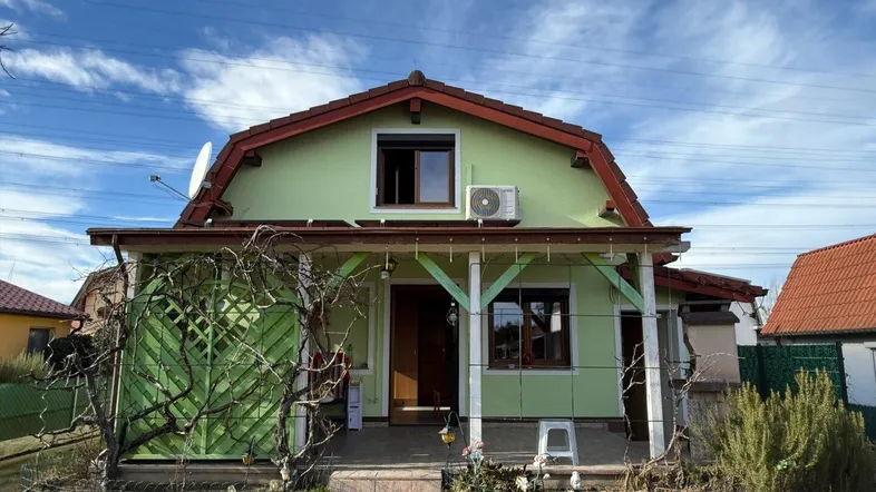 Grünes Einfamilienhaus mit überdachtem Eingangsbereich, Garten und Klimaanlage an der Fassade.