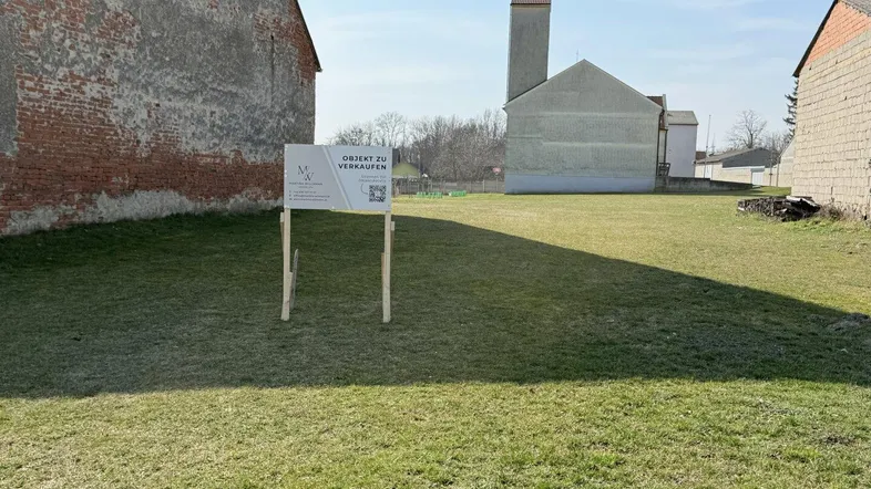 Weitläufiges Grundstück mit Verkaufsanzeige und umliegenden Gebäuden unter blauem Himmel.