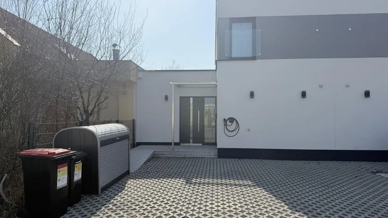 Moderne Hausfassade mit gepflasterter Einfahrt, Mülltonnenbox und französischem Balkon.