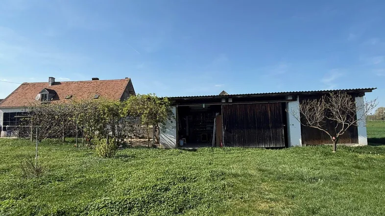 Ländliches Anwesen mit Wohnhaus und angrenzendem Scheunengebäude, umgeben von einer grünen Wiese.