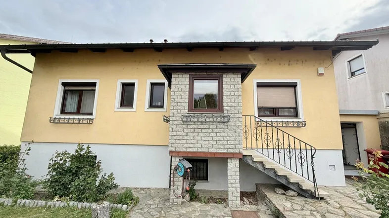 Gelbe Hausfassade mit braunen Fensterrahmen, Rollläden und Außentreppe zum Eingangsbereich.