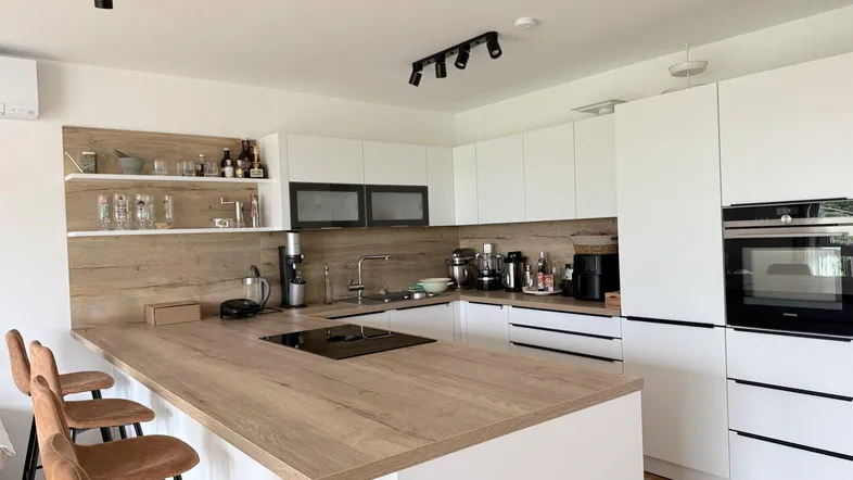 Moderne Küche mit Kochinsel, integrierten Geräten und Holzakzenten, ideal für geselliges Kochen.
