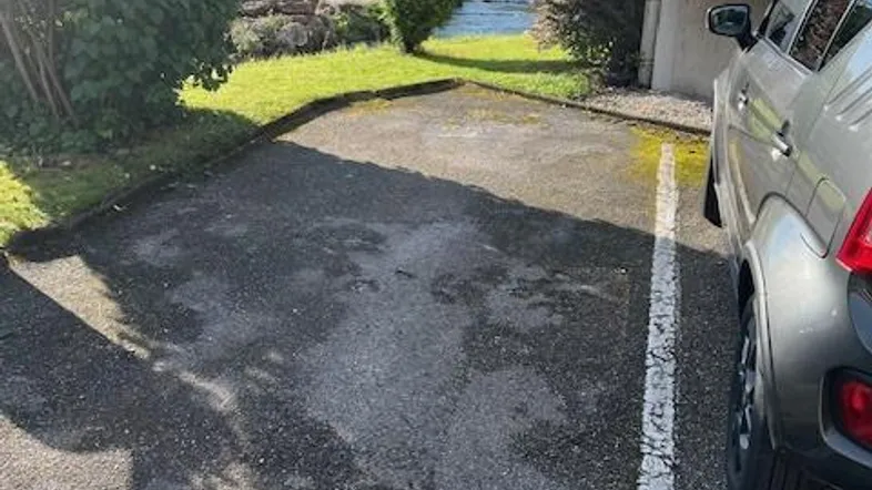 Außenbereich mit Parkplatz, Grünfläche und angrenzendem Fluss unter blauem Himmel.