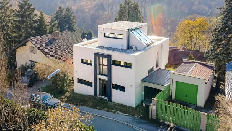Modernes Einfamilienhaus mit Flachdach, großen Fenstern und integrierter Klimaanlage in grüner Hanglage.