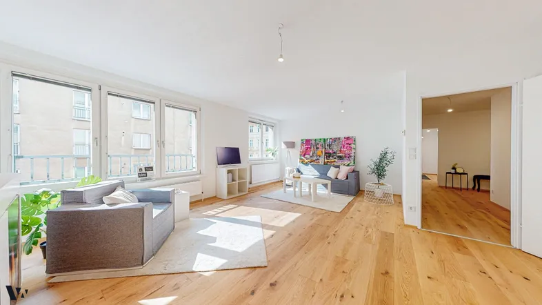 Helles und geräumiges Wohnzimmer mit Holzboden, großen Fenstern und moderner Einrichtung.