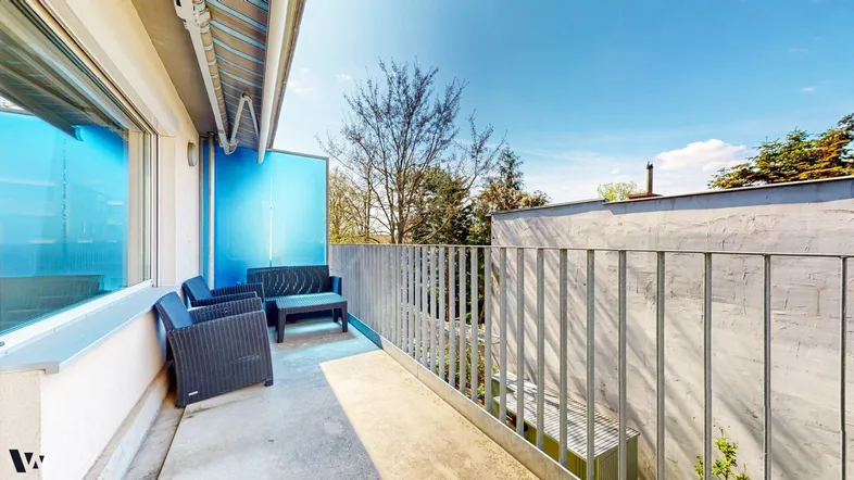Geräumiger Balkon mit Sitzgelegenheiten und einer blauen Trennwand, ideal zum Entspannen im Freien.