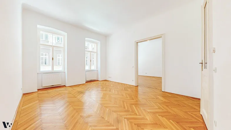 Helles, leeres Zimmer mit Fischgrätparkett und hohen Fenstern, bereit zur individuellen Gestaltung.