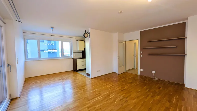 Helles Wohnzimmer mit Parkettboden und integriertem Küchenbereich, ideal für offenes Wohnen.