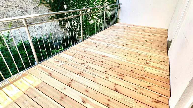 Neuer Holzbalkon mit Metallgeländer und grüner Efeuwand, ideal für entspannte Stunden im Freien.