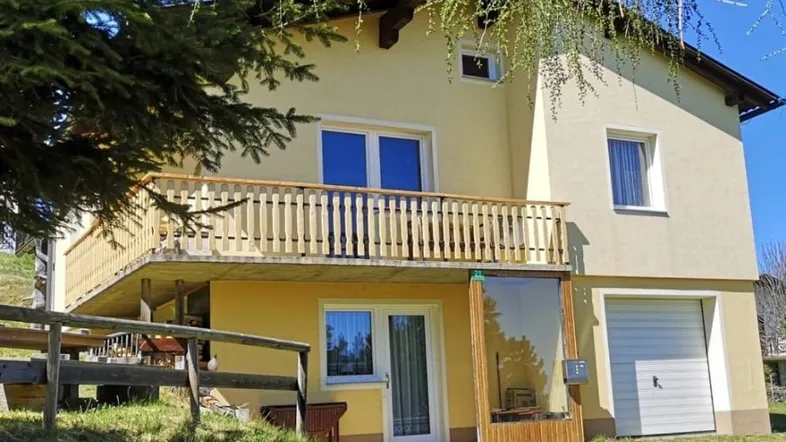 Charmantes Chalet mit Balkon und integrierter Garage, umgeben von grüner Landschaft.