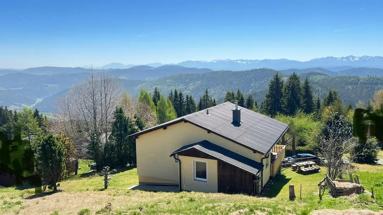 Haus in alpiner Landschaft mit weitem Blick auf bewaldete Berge und Täler.