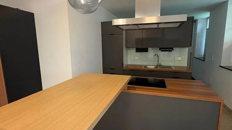 Moderne Küche mit dunklen Schränken, Holz-Arbeitsplatten und einer Kochinsel, beleuchtet von einer stilvollen Pendelleuchte.