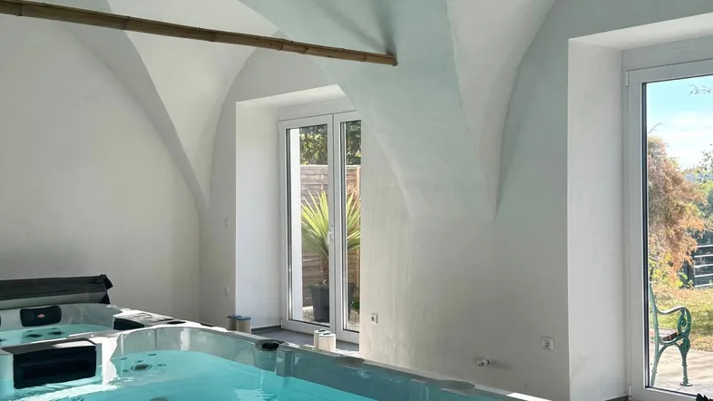 Innenbereich mit großem Swim-Spa und Whirlpool unter einem Gewölbedach mit viel Tageslicht.