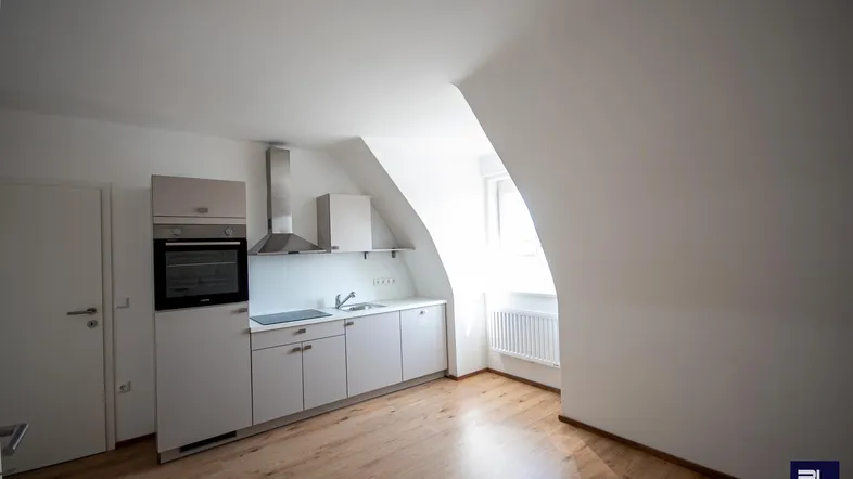 Helle Küchenzeile im Dachgeschoss mit Schrägdecke, Einbaugeräten und hellem Holzfußboden.