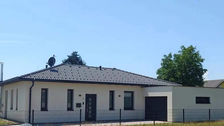 Modernes Einfamilienhaus mit dunklem Ziegeldach und heller Fassade unter blauem Himmel.