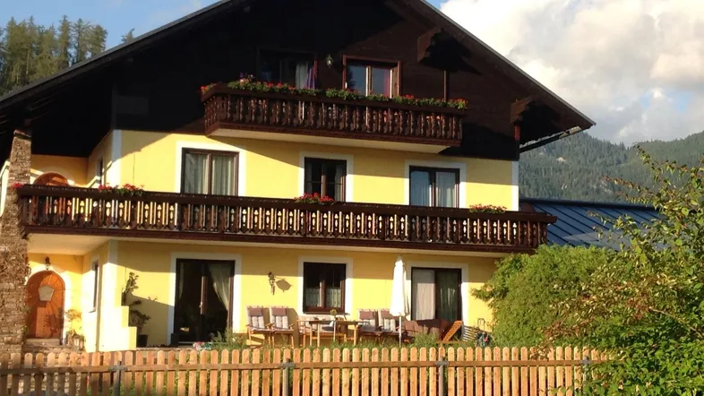 Traditionelles Haus mit gelber Fassade, Holzbalkonen und einem gepflegten Gartenbereich.
