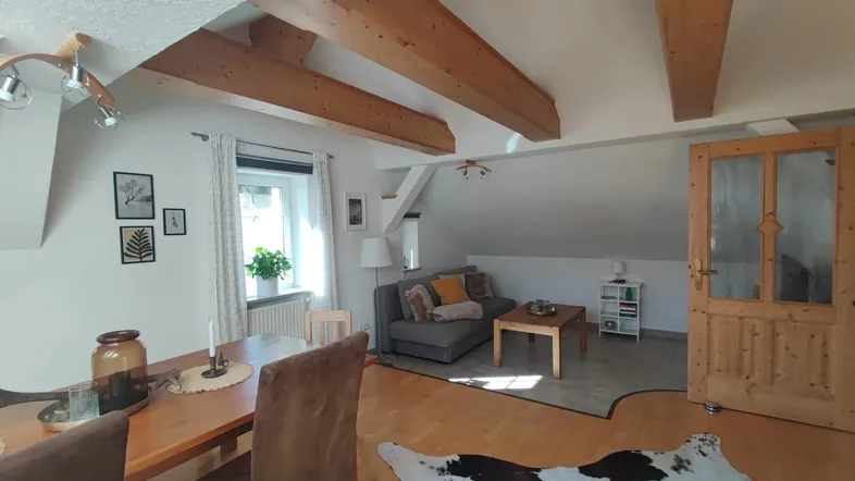 Gemütlicher Wohn-Essbereich im Dachgeschoss mit sichtbaren Holzbalken und rustikalem Charme.