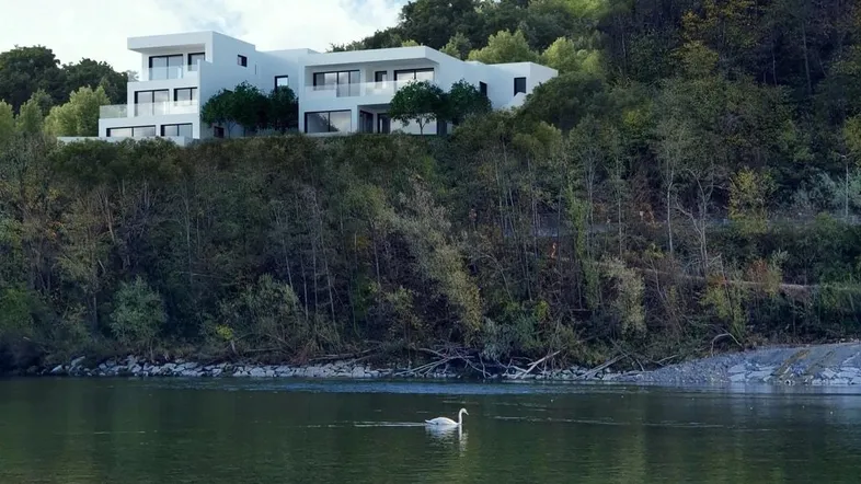 Moderne weiße Villa am Hang mit Blick auf den Fluss, umgeben von üppiger Natur.