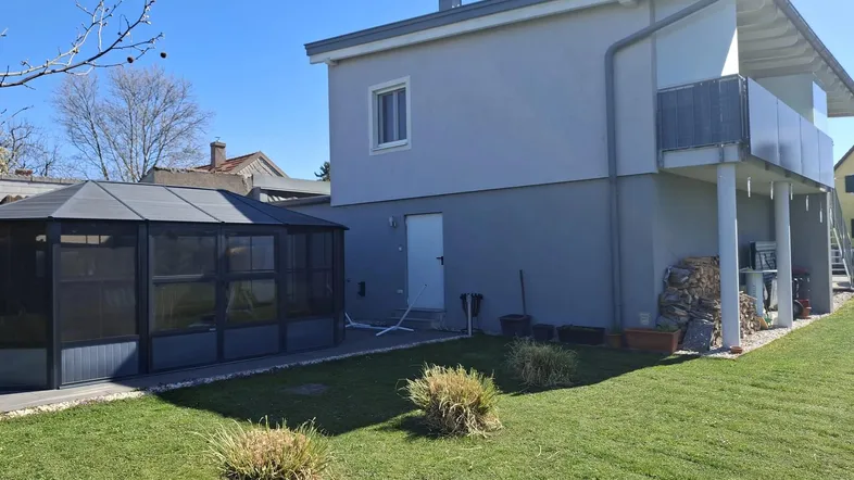 Modernes Haus mit gepflegtem Rasen, einem Wintergarten und einem kleinen Balkon im Obergeschoss.