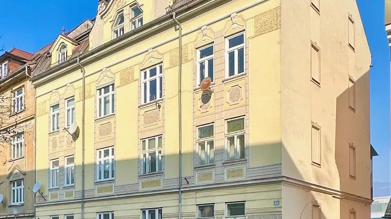 Historisches Mehrfamilienhaus mit gelber Fassade und vielen Fenstern an einer Straße.
