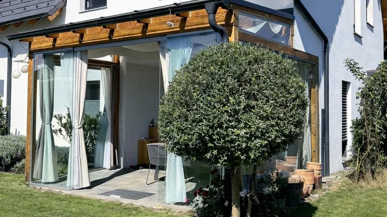 Modernes Haus mit weißer Fassade, großem Garten und verglaster Terrasse unter blauem Himmel.
