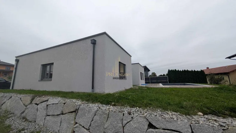 Modernes Haus mit flachem Dach, grauer Fassade und einem Steinwall im Vordergrund.