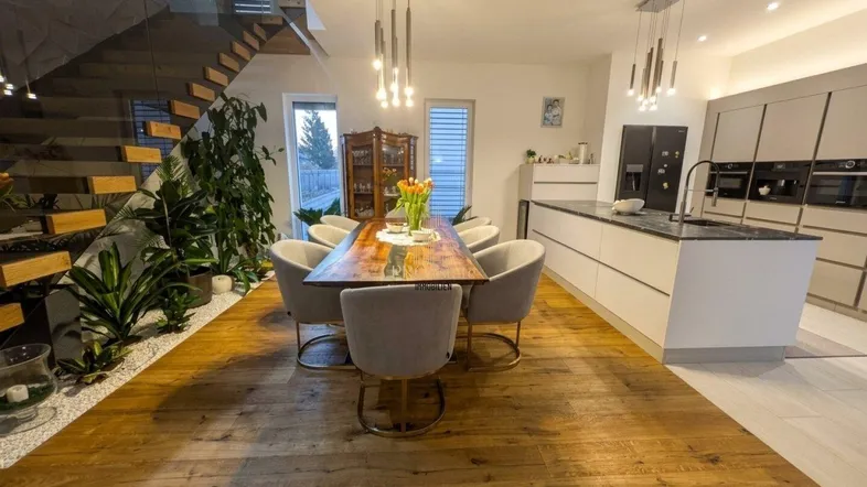 Moderner offener Wohn- und Essbereich mit Holzboden, integrierter Küche und eleganter Treppe.
